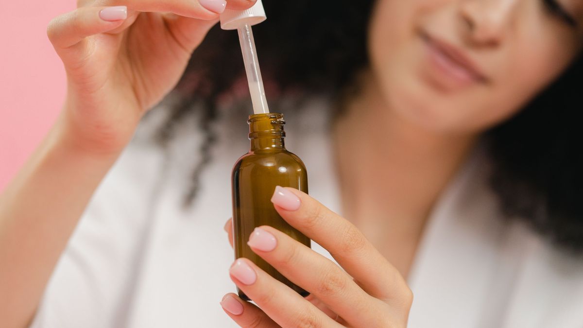 A woman holding a serum dropper up to the light