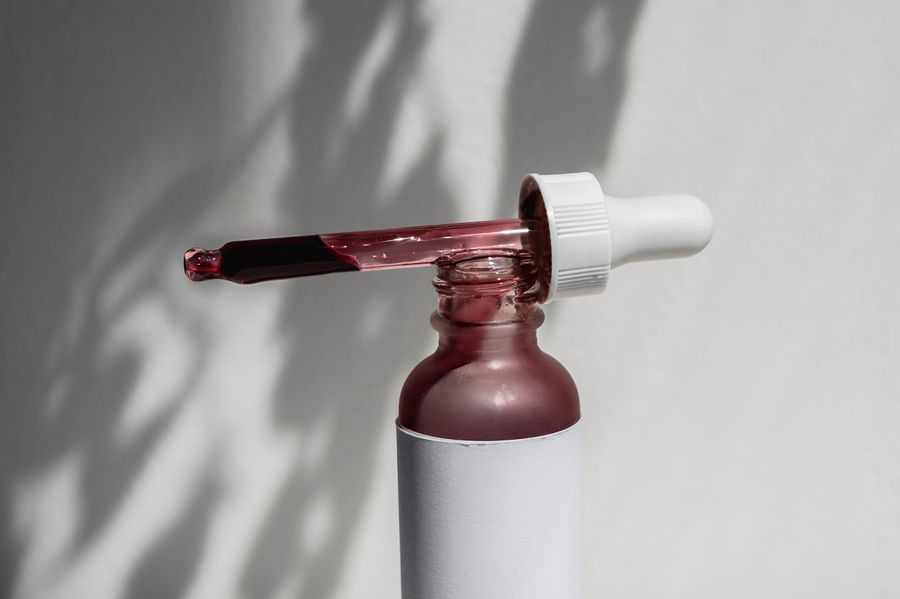 A glass dropper resting on a serum bottle in hard daylight