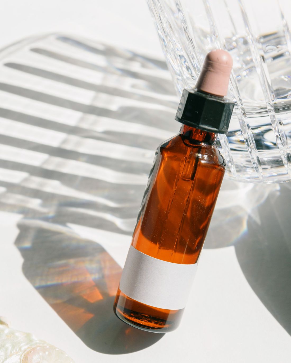 An amber serum bottle with a blank label, lit through window blinds